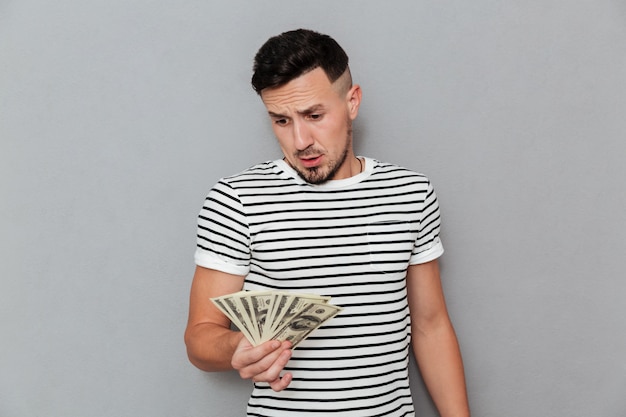 Hombre sorprendido en camiseta sosteniendo y mirando el dinero