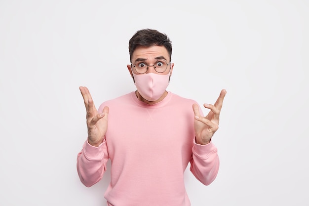 El hombre sorprendido y desconcertado levanta la mano, parece indignado, se pregunta por qué sucedió, por lo que usa una máscara protectora durante la propagación del coronavirus vestido con un jersey informal