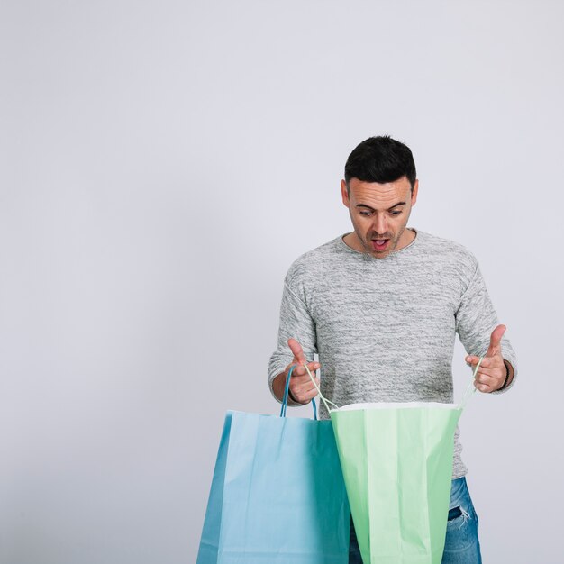 Hombre sorprendido mirando en bolsas de compra