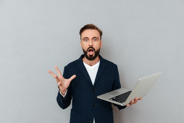 Hombre sorprendido mirando la cámara mientras sostiene la computadora portátil