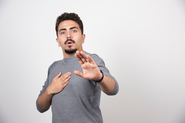 Un hombre sorprendido posando con las manos sobre una pared blanca.