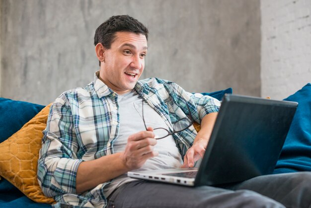 Hombre sorprendido que usa la computadora portátil en el sofá