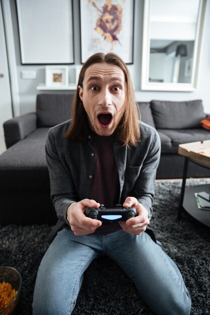 Hombre sorprendido sentado en su casa en el interior jugar con joystick