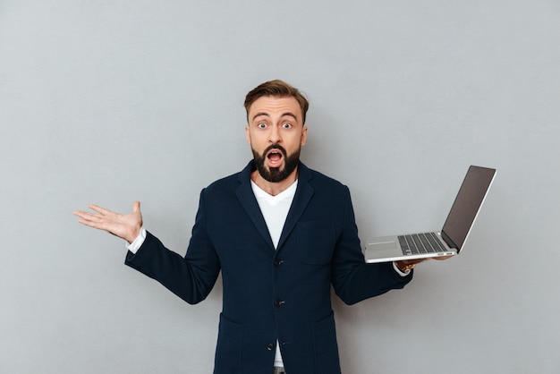 Hombre sorprendido sosteniendo la computadora portátil y mirando la cámara con la boca abierta aislada