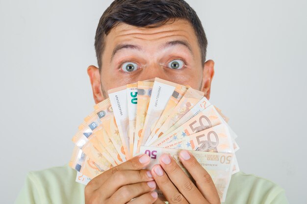 Hombre sosteniendo billetes en euros en camiseta y mirando conmocionado.