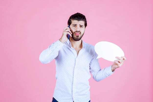 Hombre sosteniendo un bocadillo de diálogo ovale y hablando por teléfono.