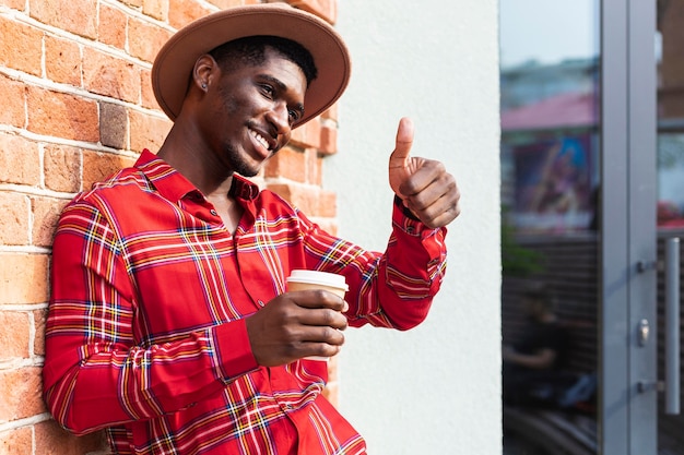 Hombre sosteniendo un café y haciendo el gesto de pulgar hacia arriba