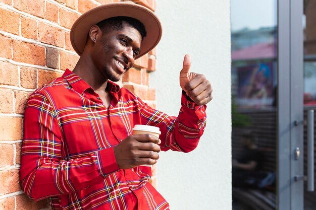 Hombre sosteniendo un café y haciendo el gesto de pulgar hacia arriba