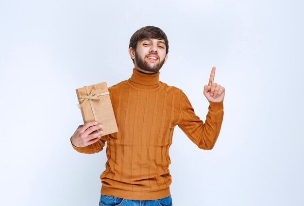 Hombre sosteniendo una caja de regalo de cartón y apuntando algo al alza.