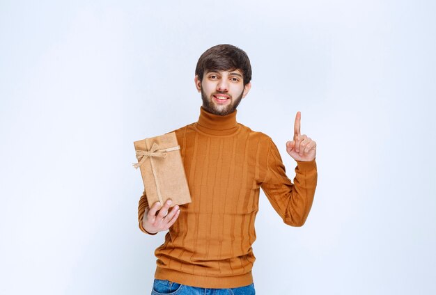 Hombre sosteniendo una caja de regalo de cartón y apuntando algo al alza.