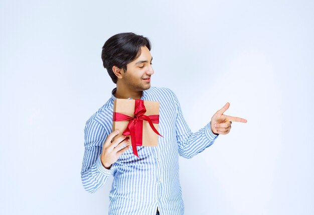 Hombre sosteniendo una caja de regalo de cartón de cinta roja y apuntando a alguien. Foto de alta calidad