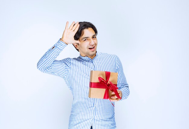 Hombre sosteniendo una caja de regalo de cartón de cinta roja y expresando su gratitud. Foto de alta calidad