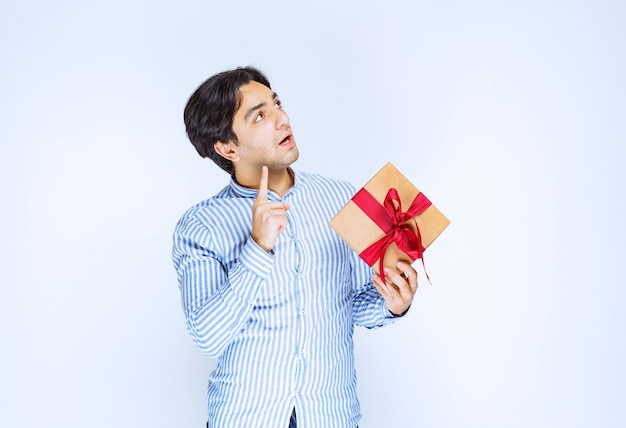 Hombre sosteniendo una caja de regalo de cartón con cinta roja y pensando en tomar una decisión. Foto de alta calidad