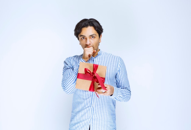 Hombre sosteniendo una caja de regalo de cartón de cinta roja y tosiendo para llamar la atención. Foto de alta calidad