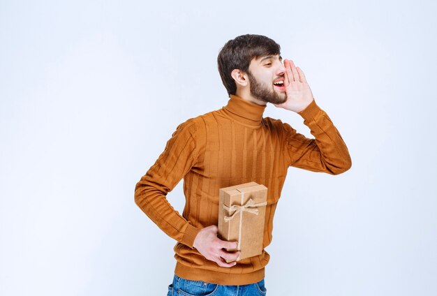 Hombre sosteniendo una caja de regalo de cartón y llamando a alguien del lado derecho.