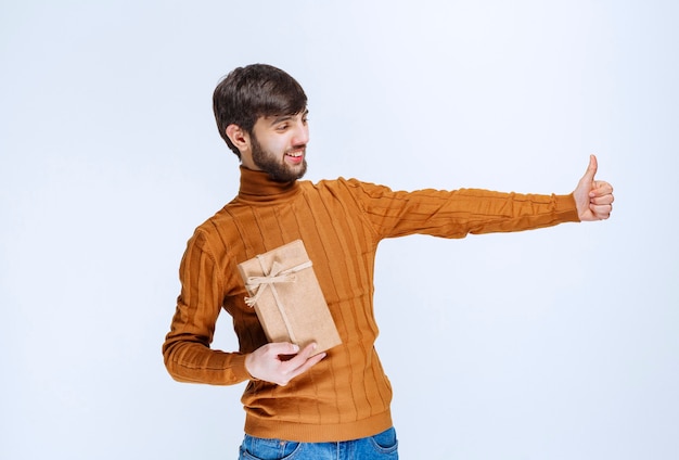 Hombre sosteniendo una caja de regalo de cartón y mostrando el signo de disfrute.