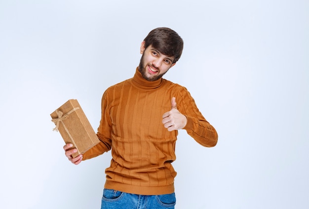 Hombre sosteniendo una caja de regalo de cartón y mostrando el signo de disfrute.