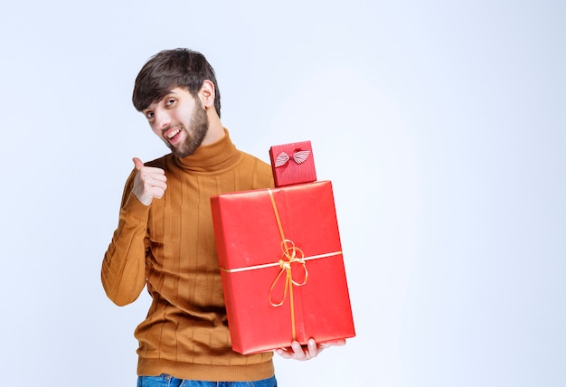 Hombre sosteniendo cajas de regalo rojas grandes y pequeñas y disfrutándolo.