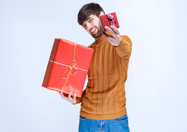 Hombre sosteniendo cajas de regalo rojas grandes y pequeñas y ofreciendo una de ellas a su novia.