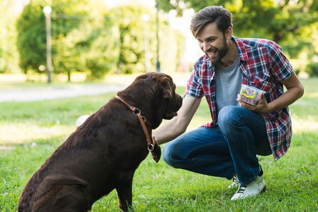 Hombre sosteniendo comida en un recipiente jugando con perro