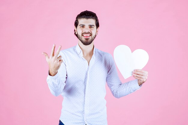 Hombre sosteniendo una figura de corazón en blanco y apuntando a ella.