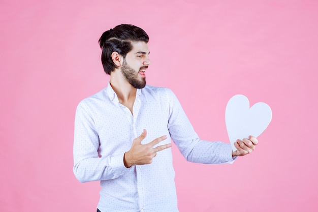 Foto gratuita hombre sosteniendo una figura de corazón en blanco y apuntando a ella.