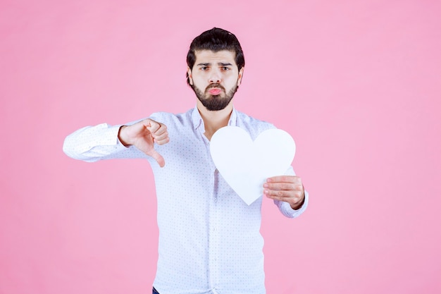 Hombre sosteniendo una figura de corazón en blanco y mostrando el pulgar hacia abajo.