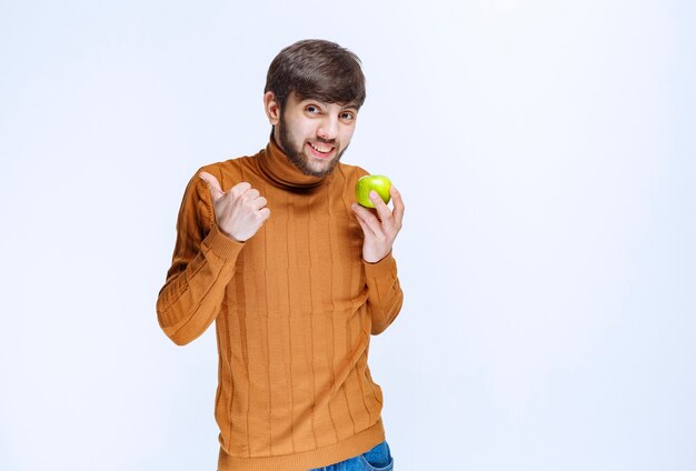 Hombre sosteniendo una manzana verde y mostrando el pulgar hacia arriba.