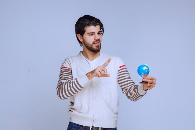 Hombre sosteniendo un mini globo, agitándolo y tratando de adivinar una ubicación.