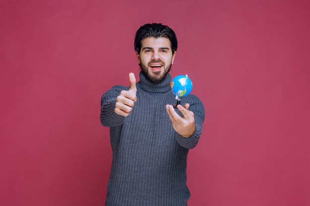 Hombre sosteniendo un mini globo y mostrando el pulgar hacia arriba.