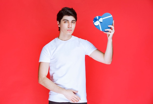 Hombre sosteniendo y ofreciendo una caja de regalo azul en forma de corazón.