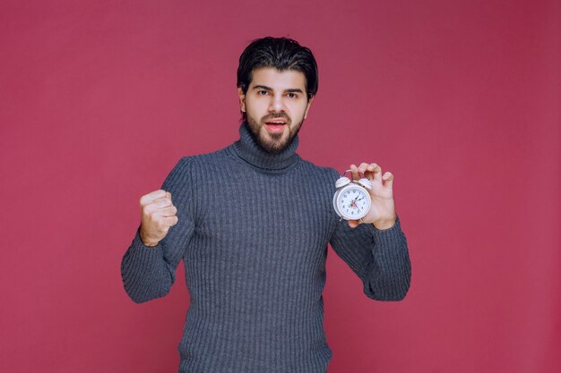 Hombre sosteniendo un reloj despertador y mostrando su puño.