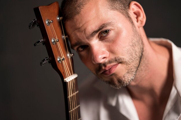 Hombre sosteniendo su cabeza en el clavijero de la guitarra y mirando