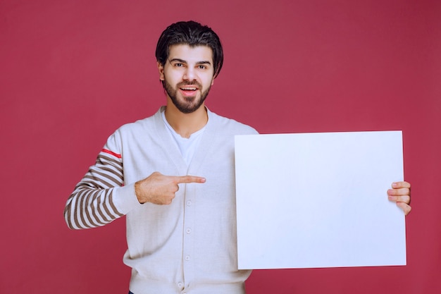 Hombre sosteniendo un tablero de ideas en blanco y apuntando hacia él para llamar la atención.