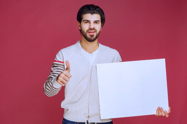 Hombre sosteniendo un tablero de ideas en blanco y haciendo pulgar hacia arriba.