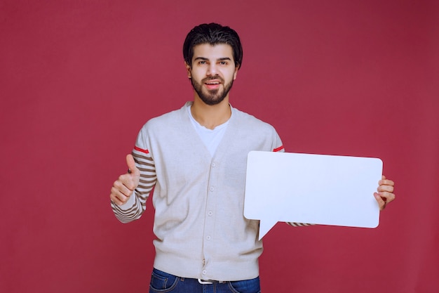 Hombre sosteniendo un tablero de ideas en blanco y haciendo pulgar hacia arriba.