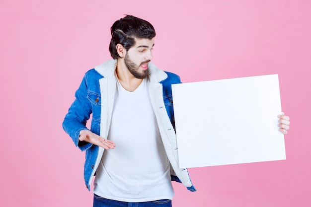 Hombre sosteniendo un tablero de ideas cuadrado en blanco y apuntando a él