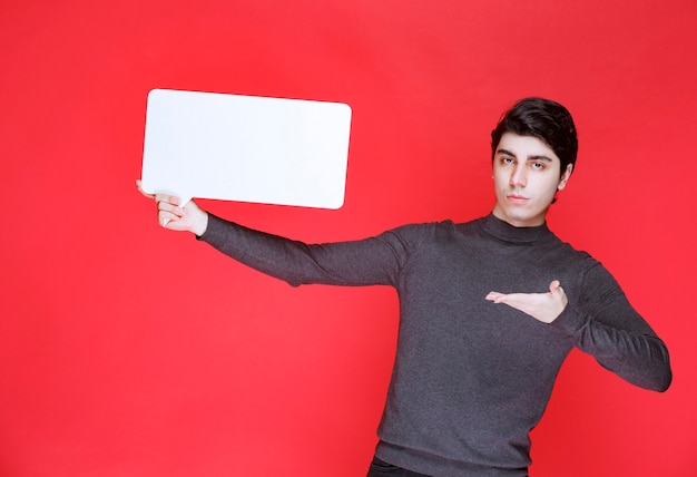 Hombre sosteniendo un tablero de ideas rectangular y apuntando a los participantes