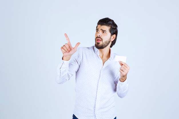 Hombre sosteniendo una tarjeta de visita y apuntando a alguien alrededor