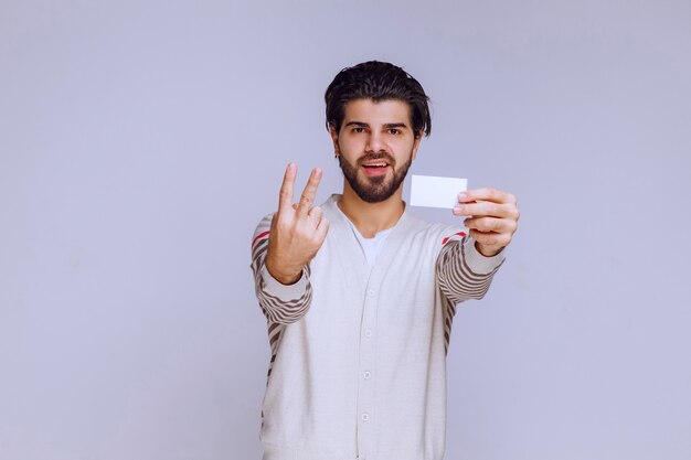 Hombre sosteniendo una tarjeta de visita y haciendo un signo de amistad.