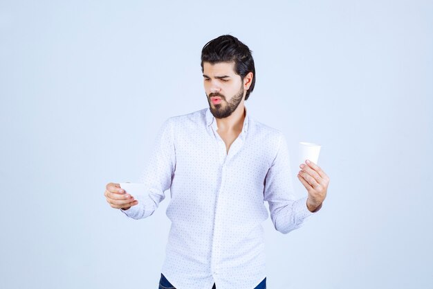 Hombre sosteniendo una taza de café y comprobando los detalles de la tarjeta de visita