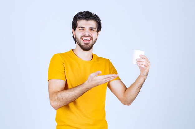 Hombre sosteniendo una taza de café y dando una presentación con la mano abierta.