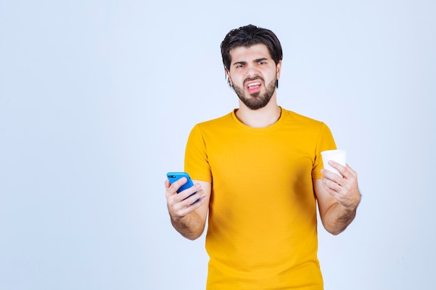 Hombre sosteniendo una taza de café y demostrando su nuevo modelo de teléfono inteligente.