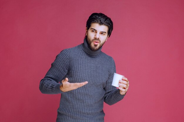 Hombre sosteniendo una taza de café desechable y apuntando a ella.