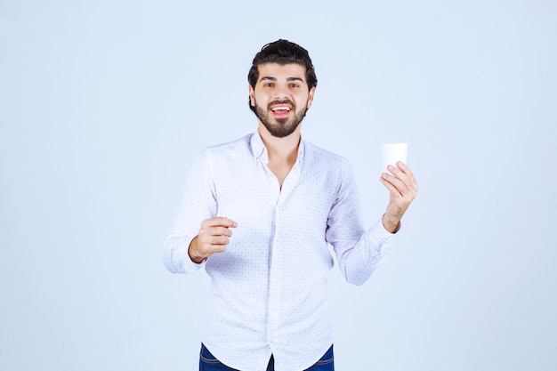 Hombre sosteniendo una taza de café en una mano y presentando su tarjeta de visita en la otra mano