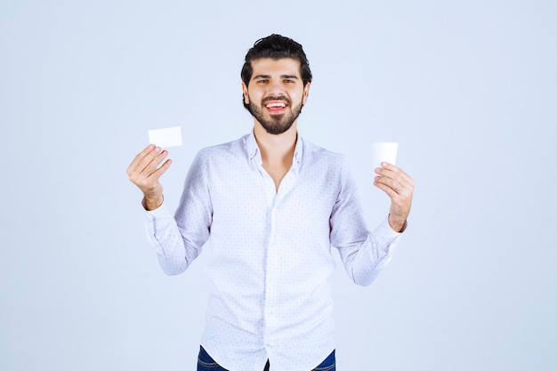 Foto gratuita hombre sosteniendo una taza de café en una mano y presentando su tarjeta de visita en la otra mano