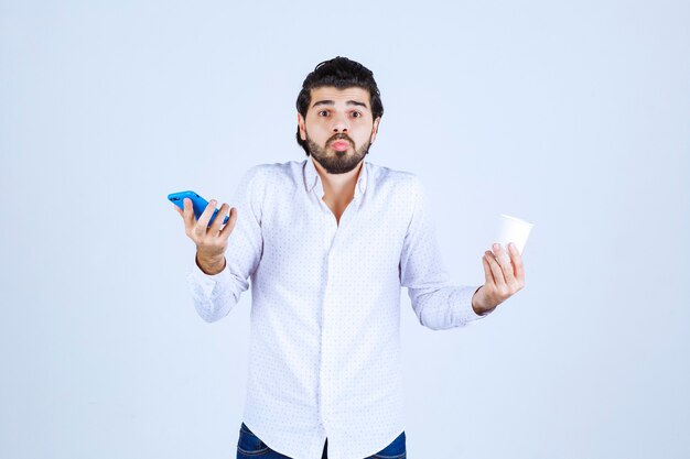 Hombre sosteniendo una taza de café en una mano y revisando su teléfono en la otra mano