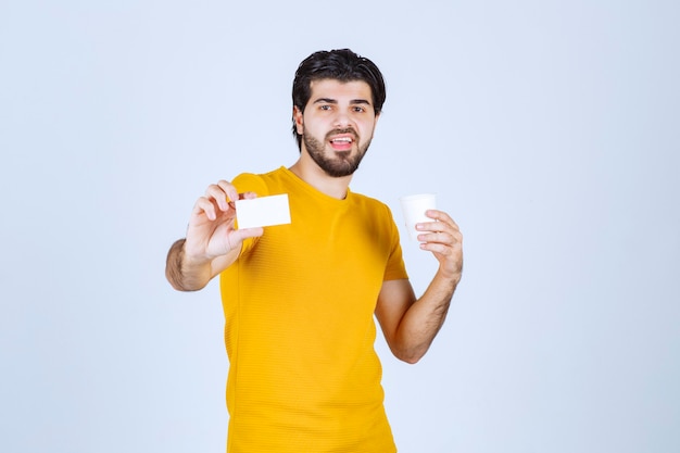 Hombre sosteniendo una taza de café y presentando su tarjeta de visita.