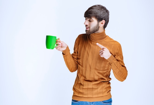 Hombre sosteniendo una taza verde y apuntando a ella.