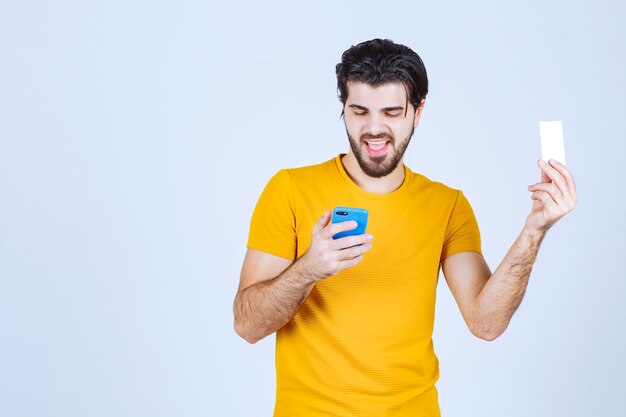 Hombre sosteniendo un teléfono inteligente azul y revisando sus mensajes o llamando al número de contacto en la tarjeta de visita.